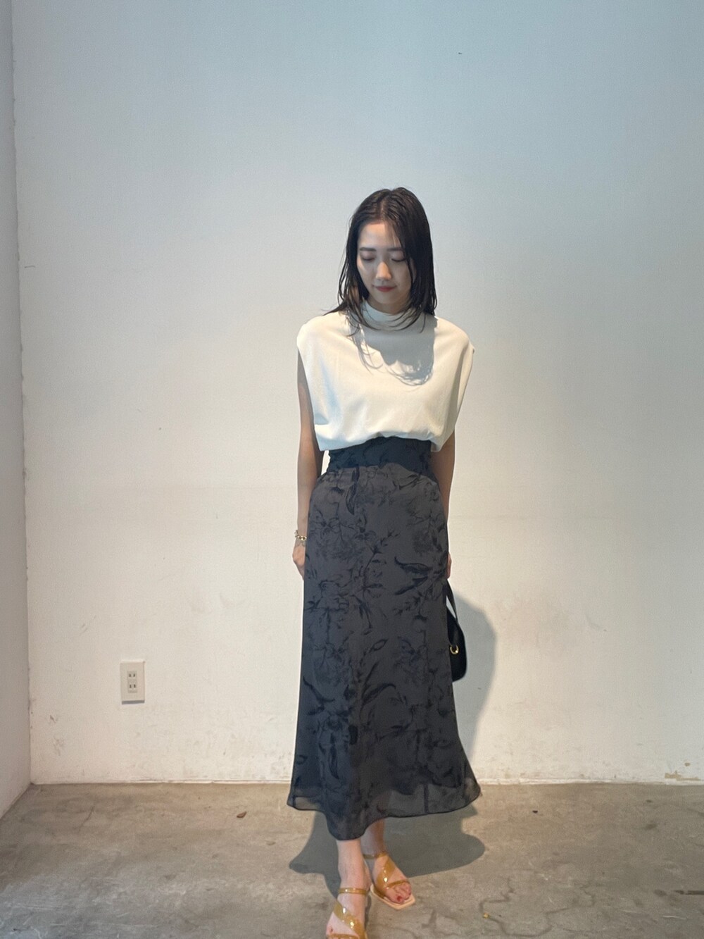 ホワイト系のニット/セーター、ブラック系のショルダーバッグ、イエロー系のサンダルを着用したレディースの夏コーディネートの2枚目の写真