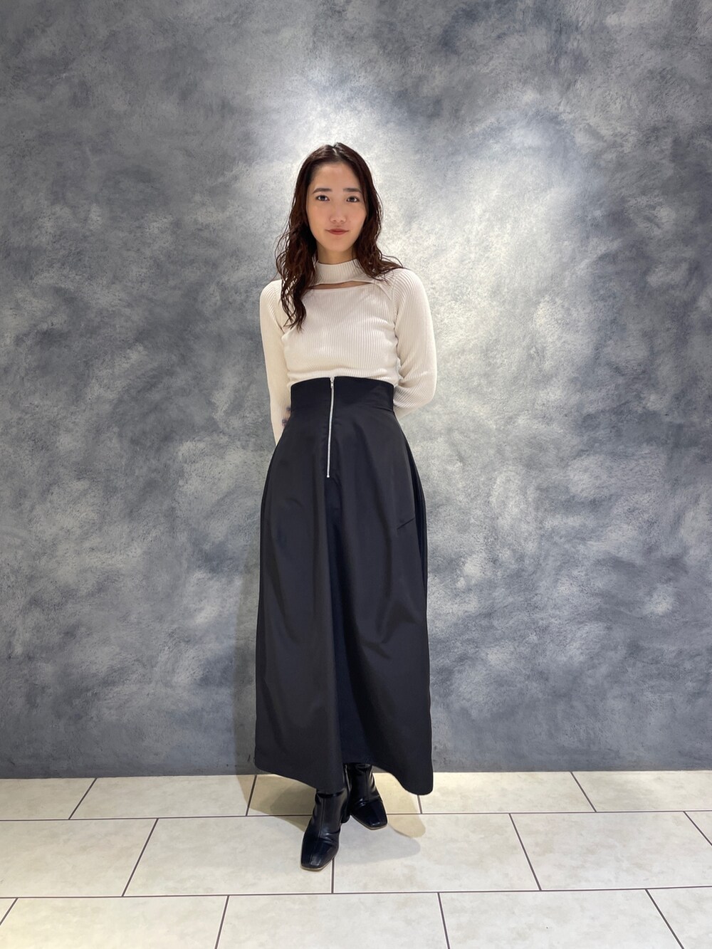 ブラック系のスカート、ホワイト系のニット/セーター、ブラック系のブーツを着用したレディースの秋コーディネートの2枚目の写真