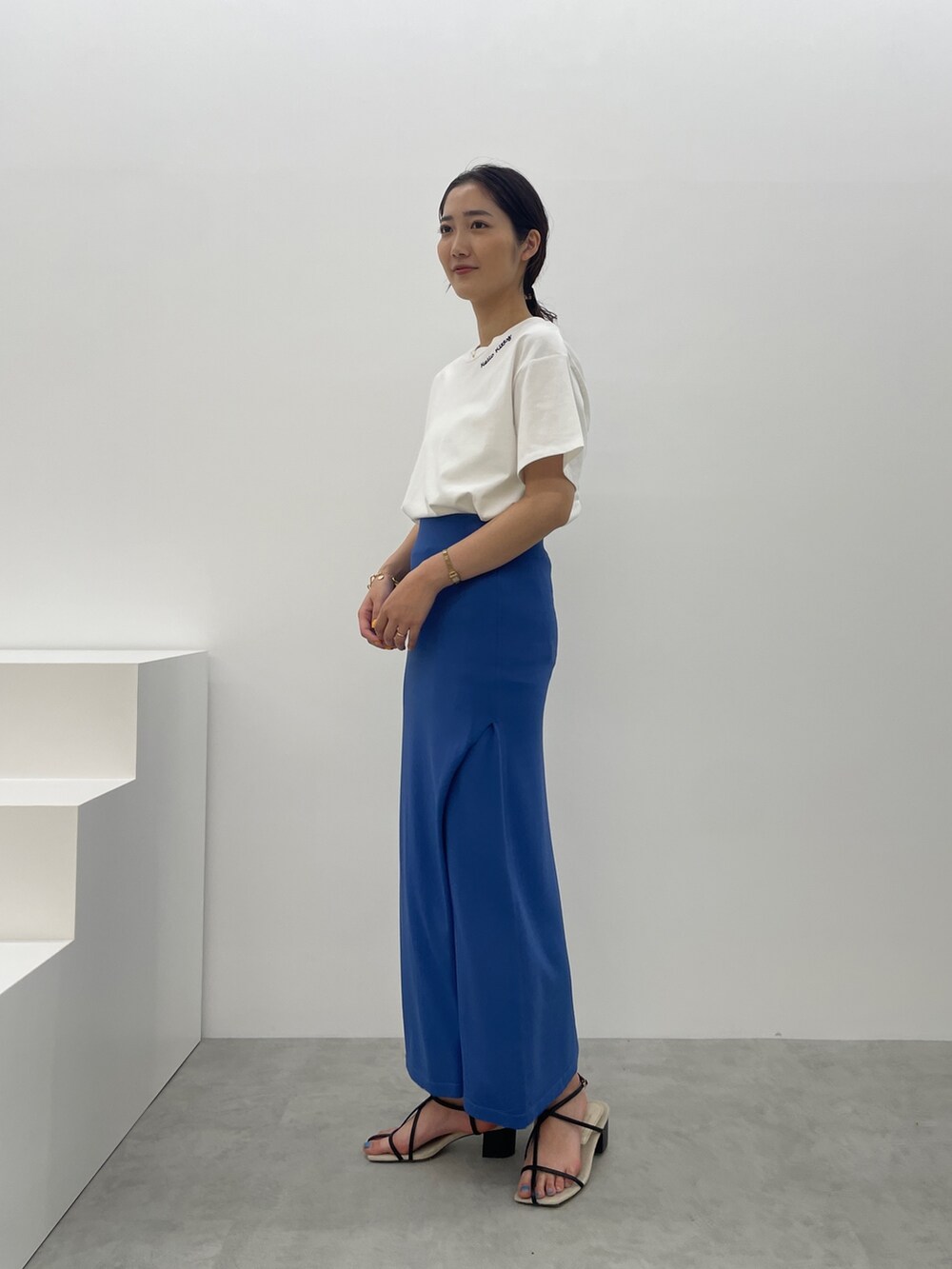 ブルー系のスカート、ホワイト系のTシャツ/カットソー、ブラック系のサンダルを着用したレディースの春コーディネートの5枚目の写真