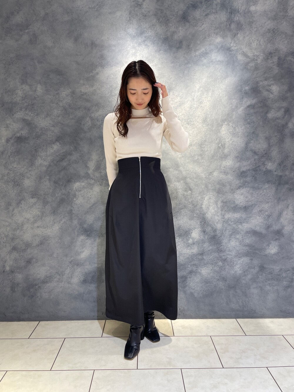 ブラック系のスカート、ホワイト系のニット/セーター、ブラック系のブーツを着用したレディースの秋コーディネートの3枚目の写真