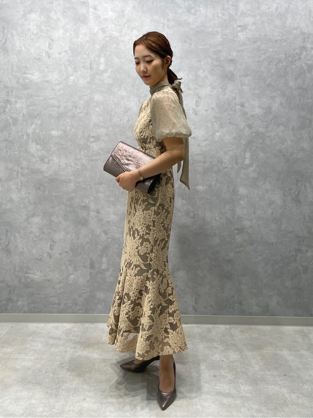 ベージュ系のドレス、シルバー系のパンプス、シルバー系のクラッチバッグを着用したレディースの夏コーディネートの3枚目の写真