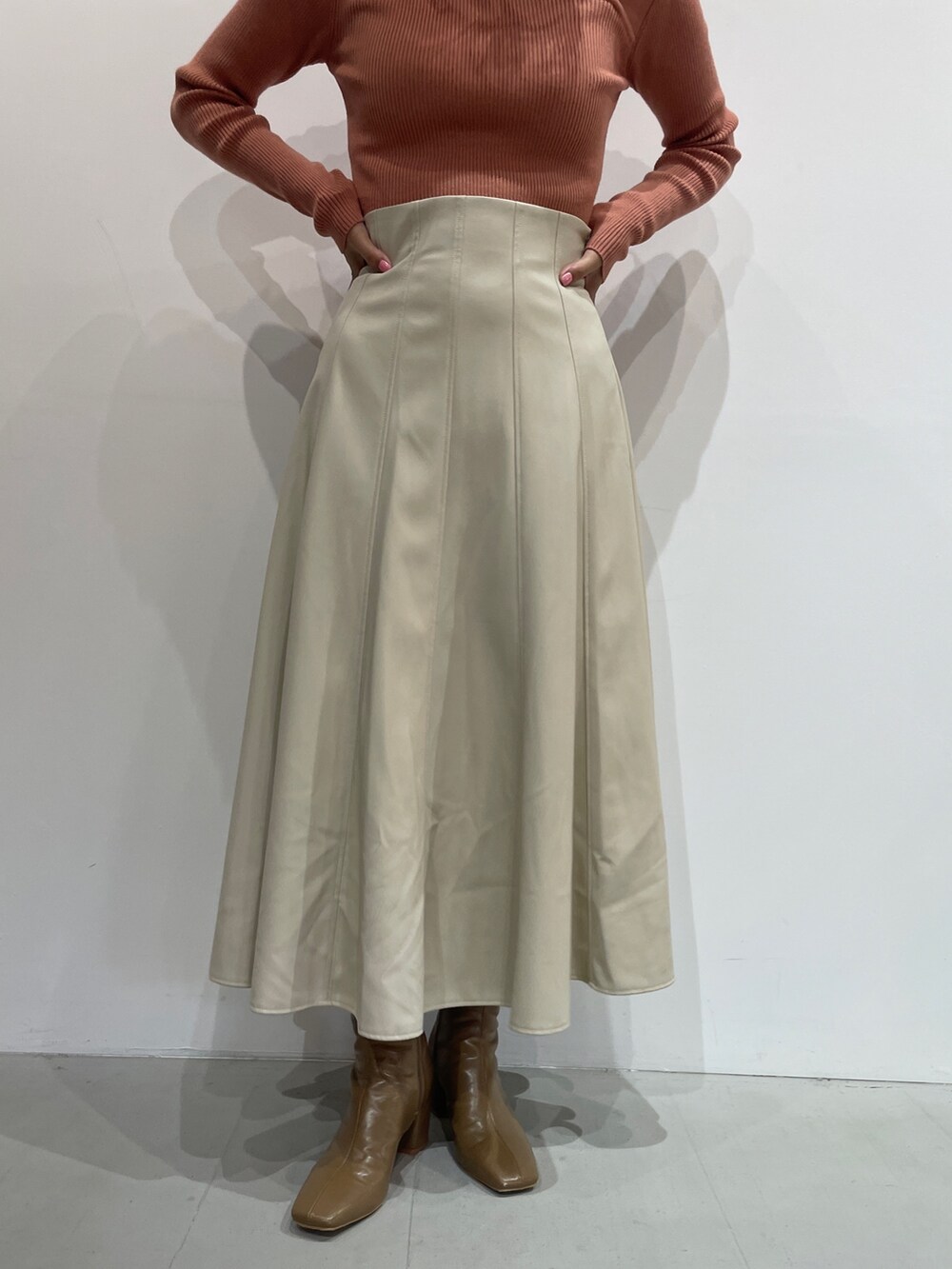 オレンジ系のニット/セーター、ホワイト系のスカート、ベージュ系のブーツを着用したレディースの秋コーディネートの6枚目の写真