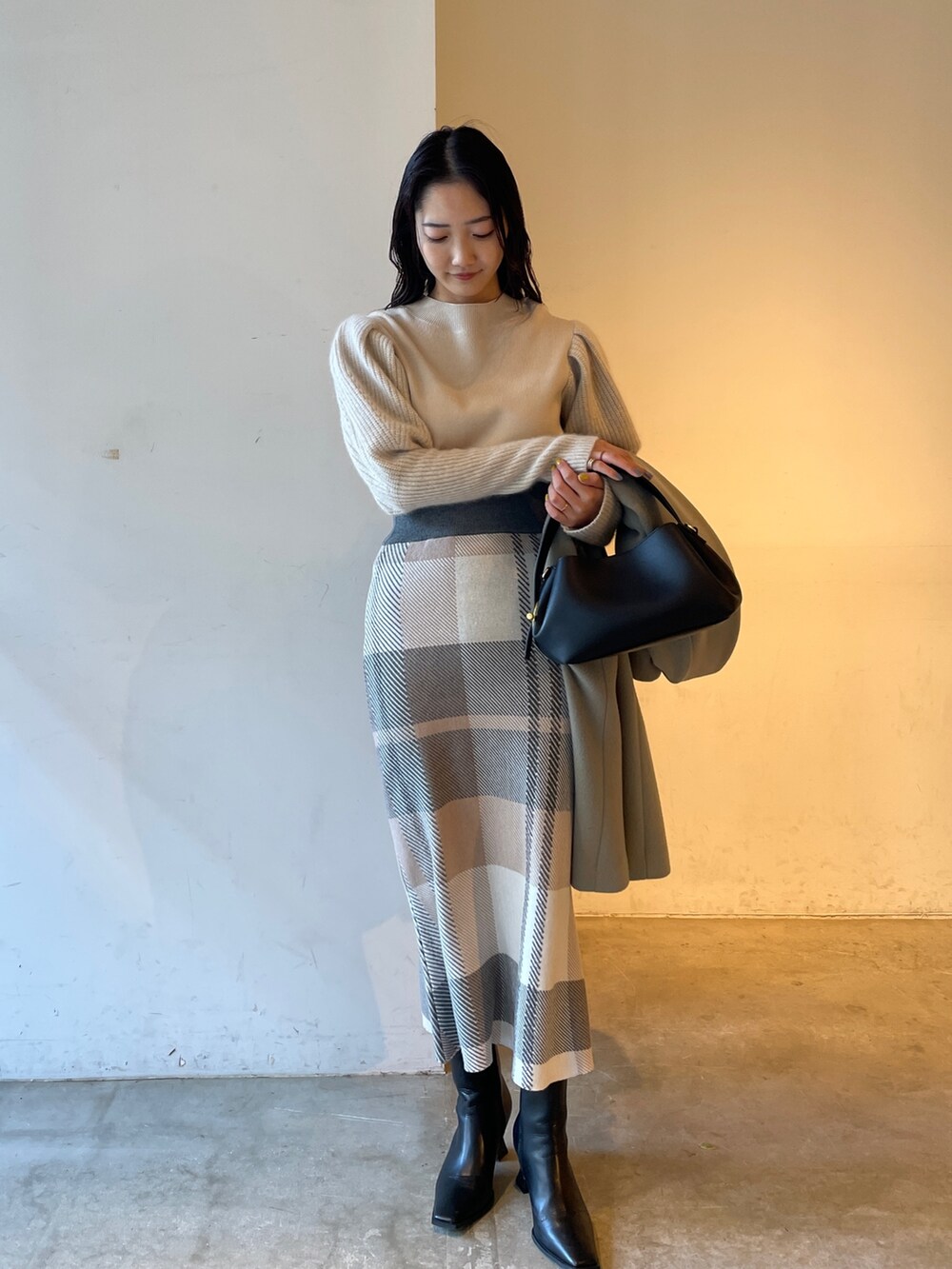 ブラック系のブーツ、ベージュ系のスカート、ホワイト系のニット/セーターを着用したレディースの冬コーディネートの2枚目の写真
