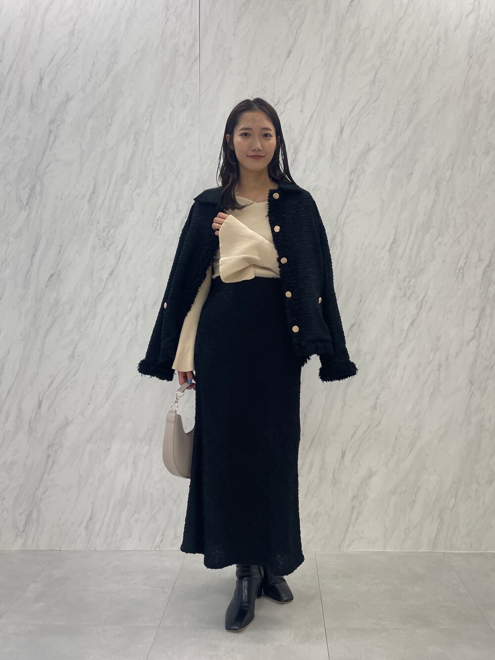 ブラック系のブーツ、ホワイト系のハンドバッグ、ブラック系のスカートを着用したレディースの秋コーディネートの3枚目の写真