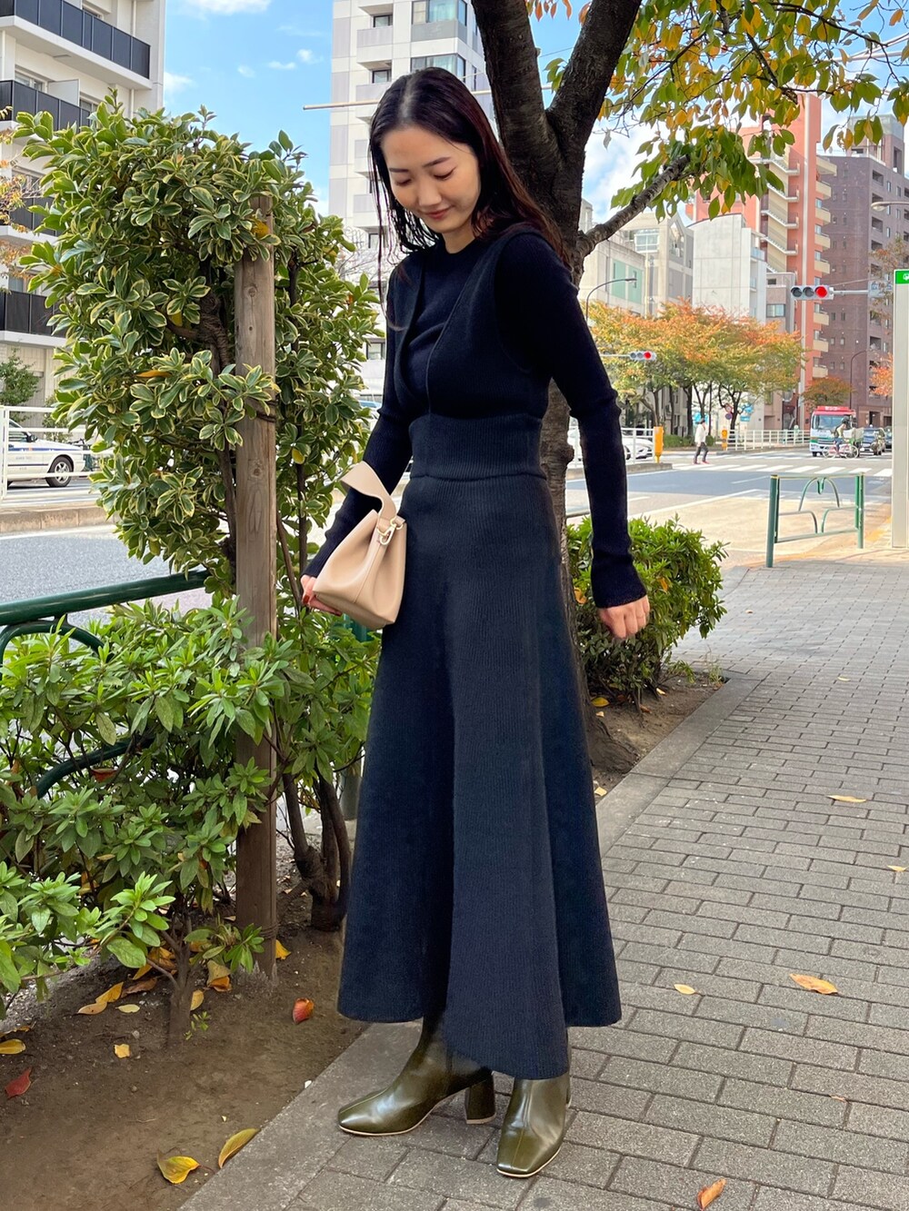 ベージュ系のハンドバッグ、グリーン系のブーツ、ブラック系のスカートを着用したレディースの秋コーディネートの2枚目の写真