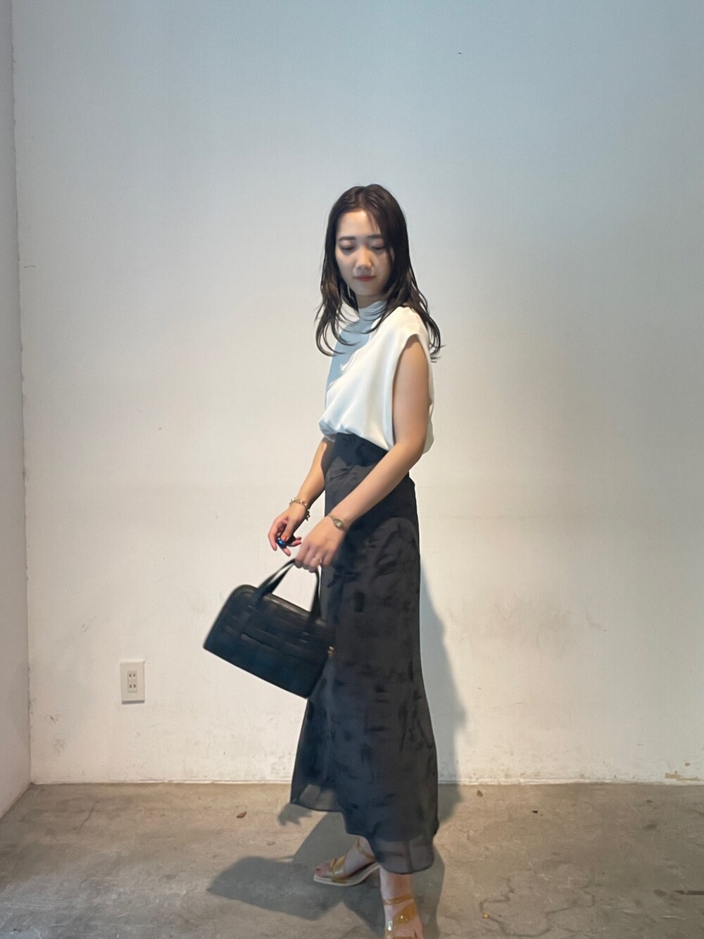 ホワイト系のニット/セーター、ブラック系のショルダーバッグ、イエロー系のサンダルを着用したレディースの夏コーディネートの3枚目の写真