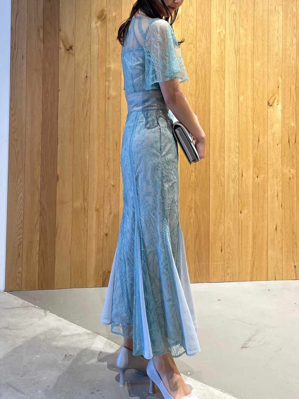 グレー系のクラッチバッグ、グレー系のパンプス、グリーン系のドレスを着用したレディースの冬コーディネートの3枚目の写真