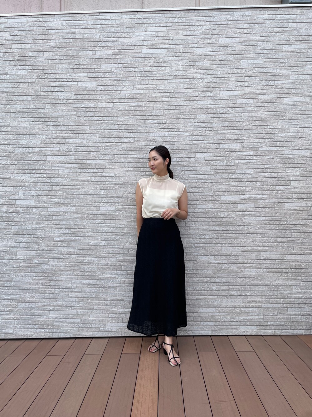 ブラック系のスカート、ホワイト系のTシャツ/カットソー、ブラック系のサンダルを着用したレディースの夏コーディネートの2枚目の写真