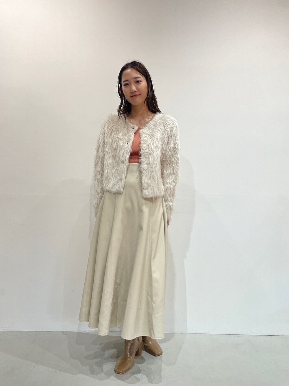 ホワイト系のスカート、ベージュ系のブーツ、オレンジ系のニット/セーターを着用したレディースの夏コーディネートの3枚目の写真