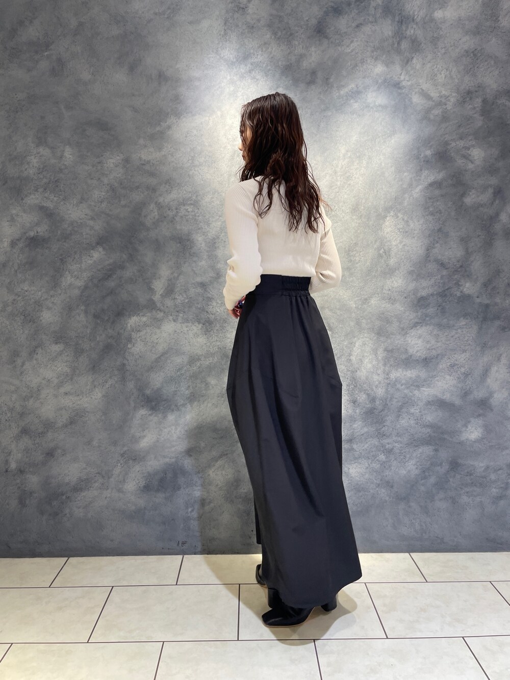 ブラック系のスカート、ホワイト系のニット/セーター、ブラック系のブーツを着用したレディースの秋コーディネートの5枚目の写真