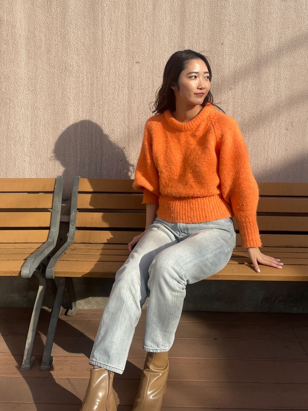 ブルー系のデニムパンツ、オレンジ系のニット/セーター、ベージュ系のブーツを着用したレディースの冬コーディネートの6枚目の写真