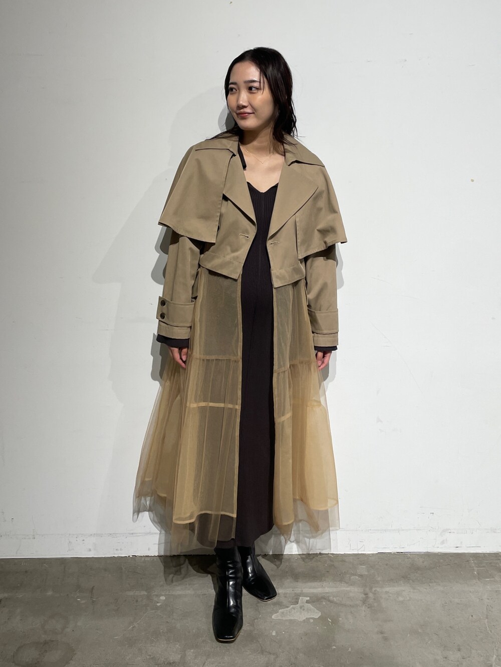 ブラック系のブーツ、グレー系のワンピース、ベージュ系のトレンチコートを着用したレディースの春コーディネートの2枚目の写真