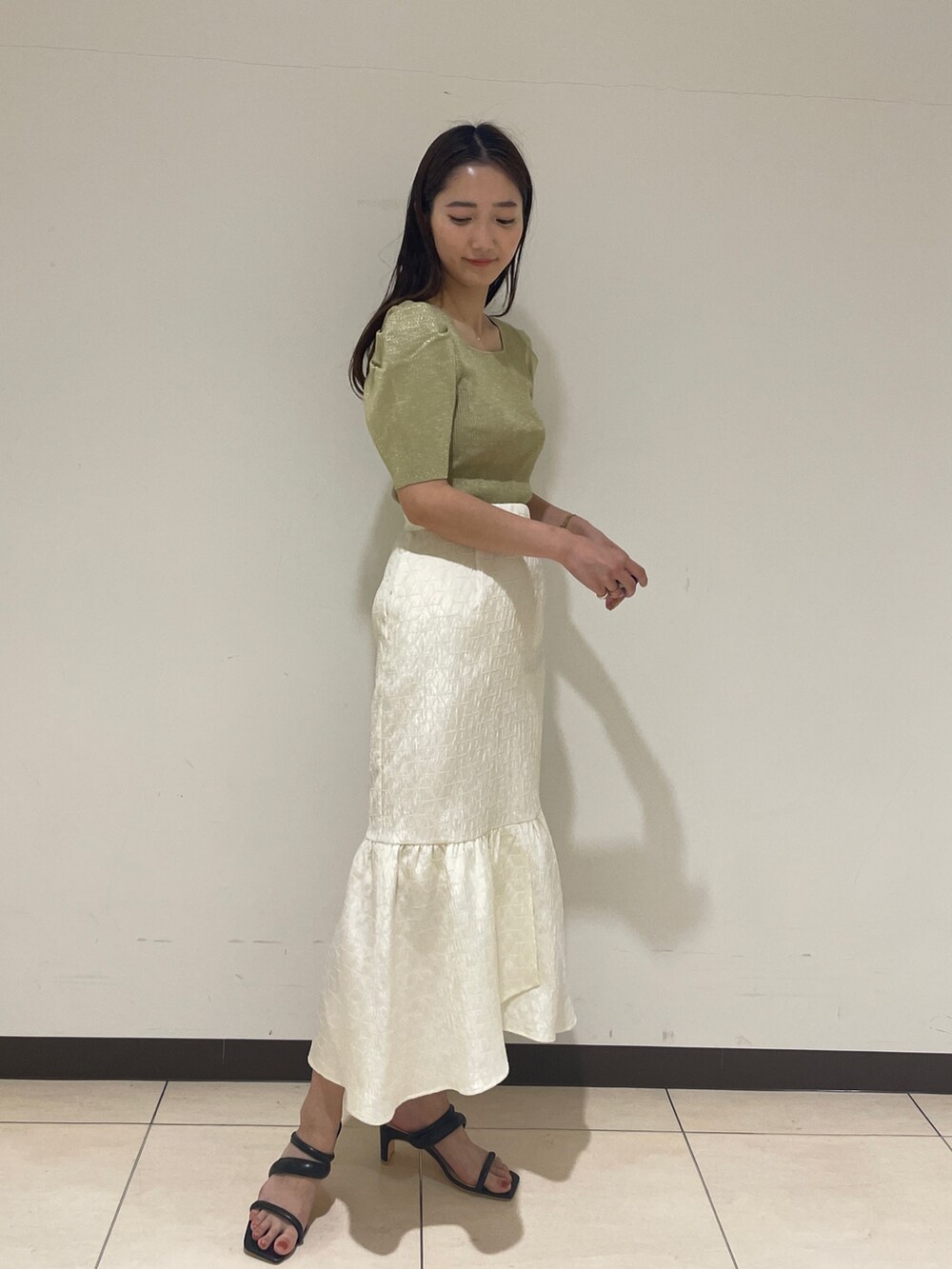 ホワイト系のスカート、グリーン系のニット/セーター、ブラック系のサンダルを着用したレディースの春コーディネートの3枚目の写真