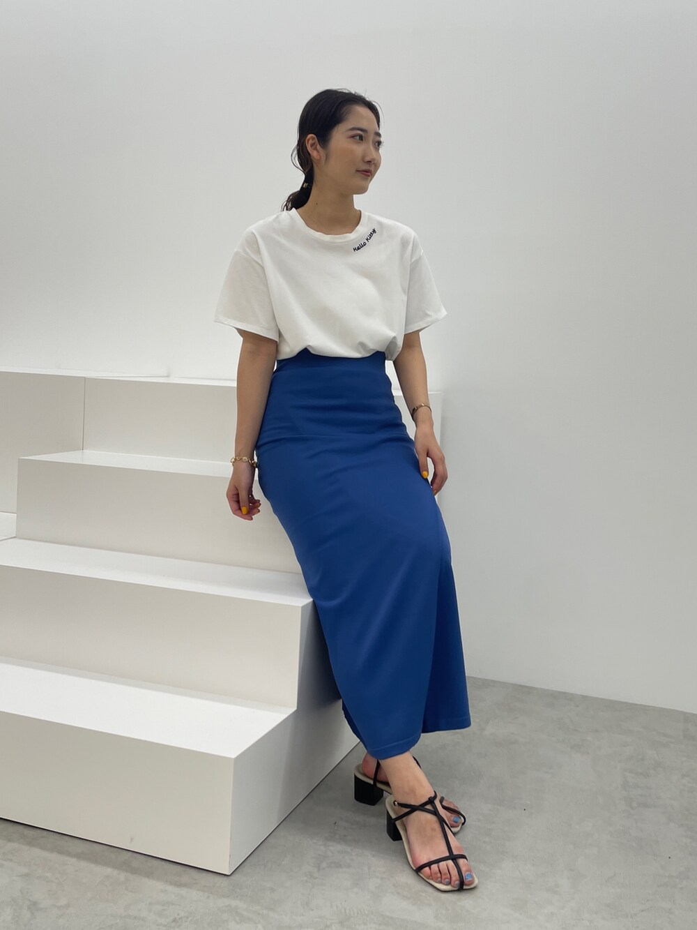 ブルー系のスカート、ホワイト系のTシャツ/カットソー、ブラック系のサンダルを着用したレディースの春コーディネートの2枚目の写真