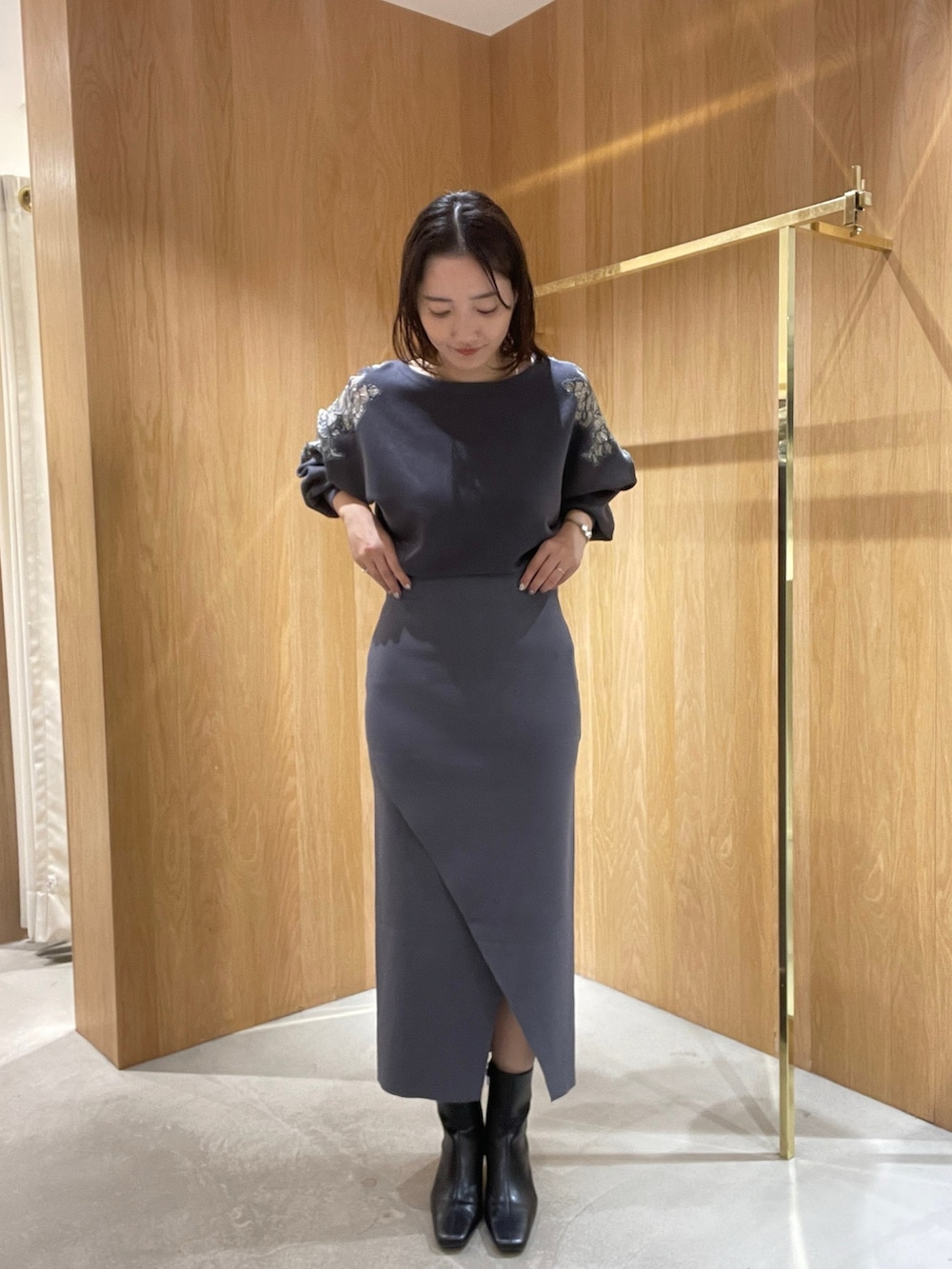 グレー系のスカート、グレー系のニット/セーター、ブラック系のブーツを着用したレディースの秋コーディネートの2枚目の写真