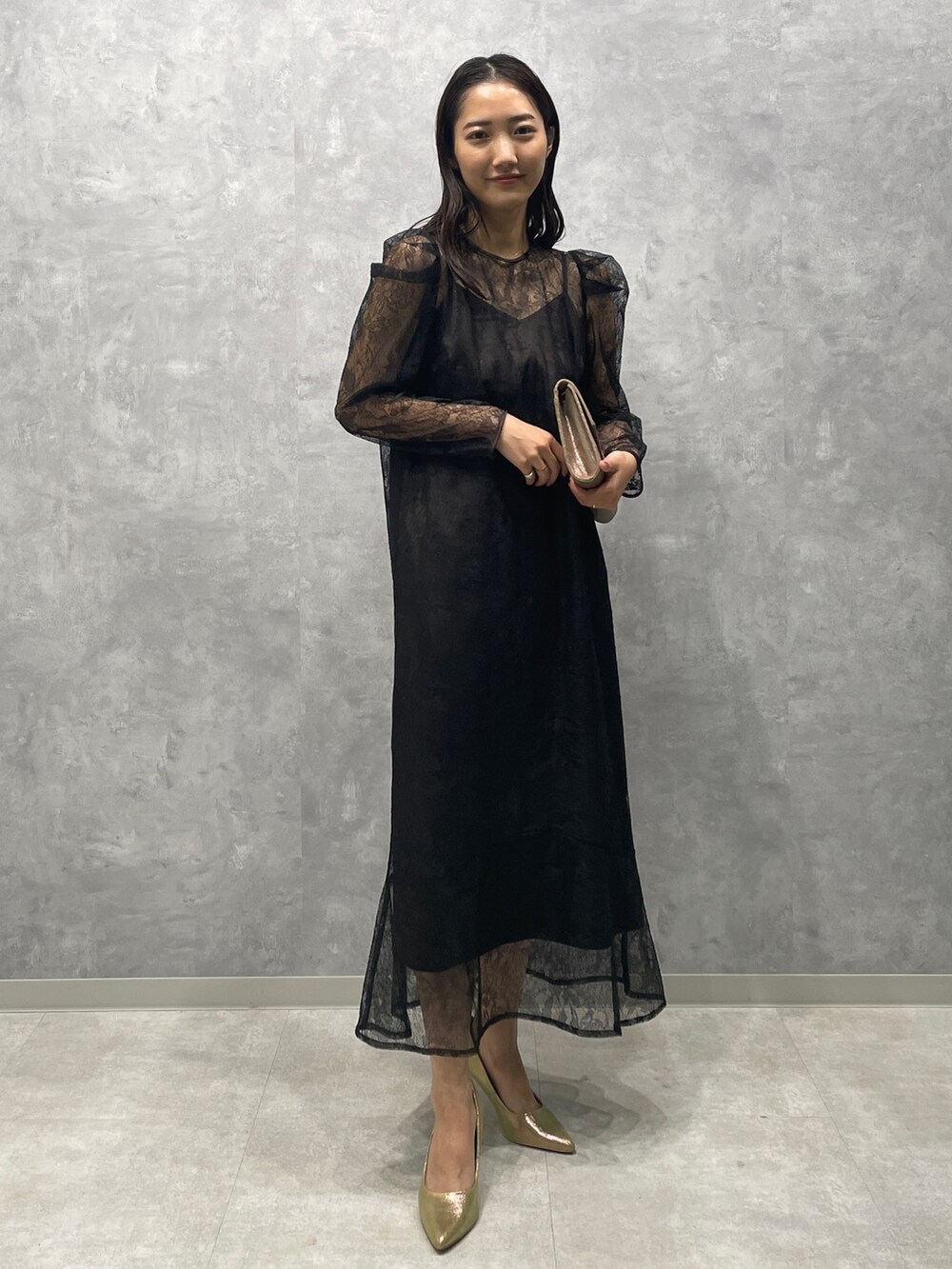 ゴールド系のパンプス、ゴールド系のハンドバッグ、ブラック系のドレスを着用したレディースの秋コーディネートの2枚目の写真