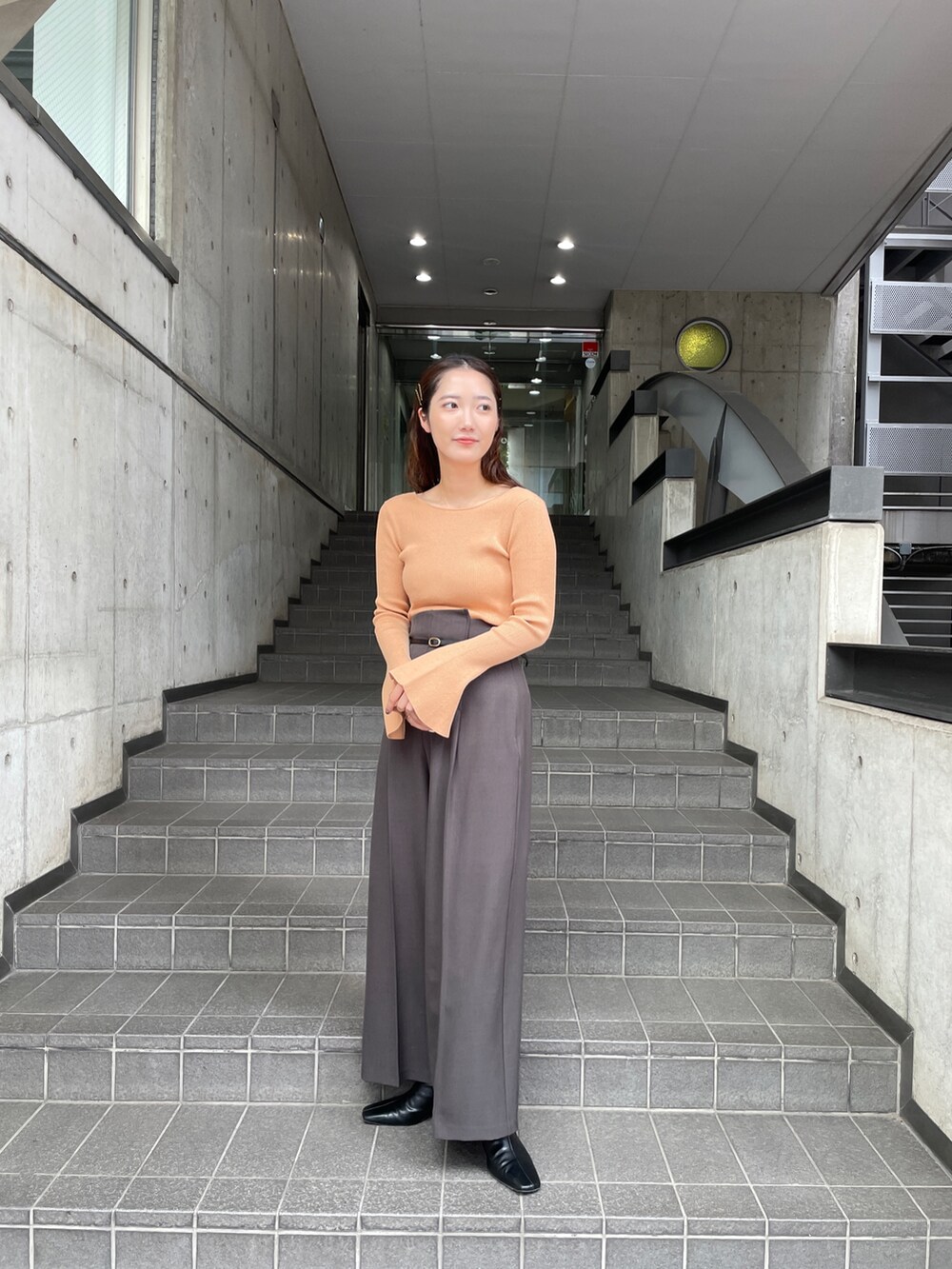 グレー系のその他パンツ、オレンジ系のニット/セーター、ブラック系のブーツを着用したレディースの秋コーディネートの3枚目の写真