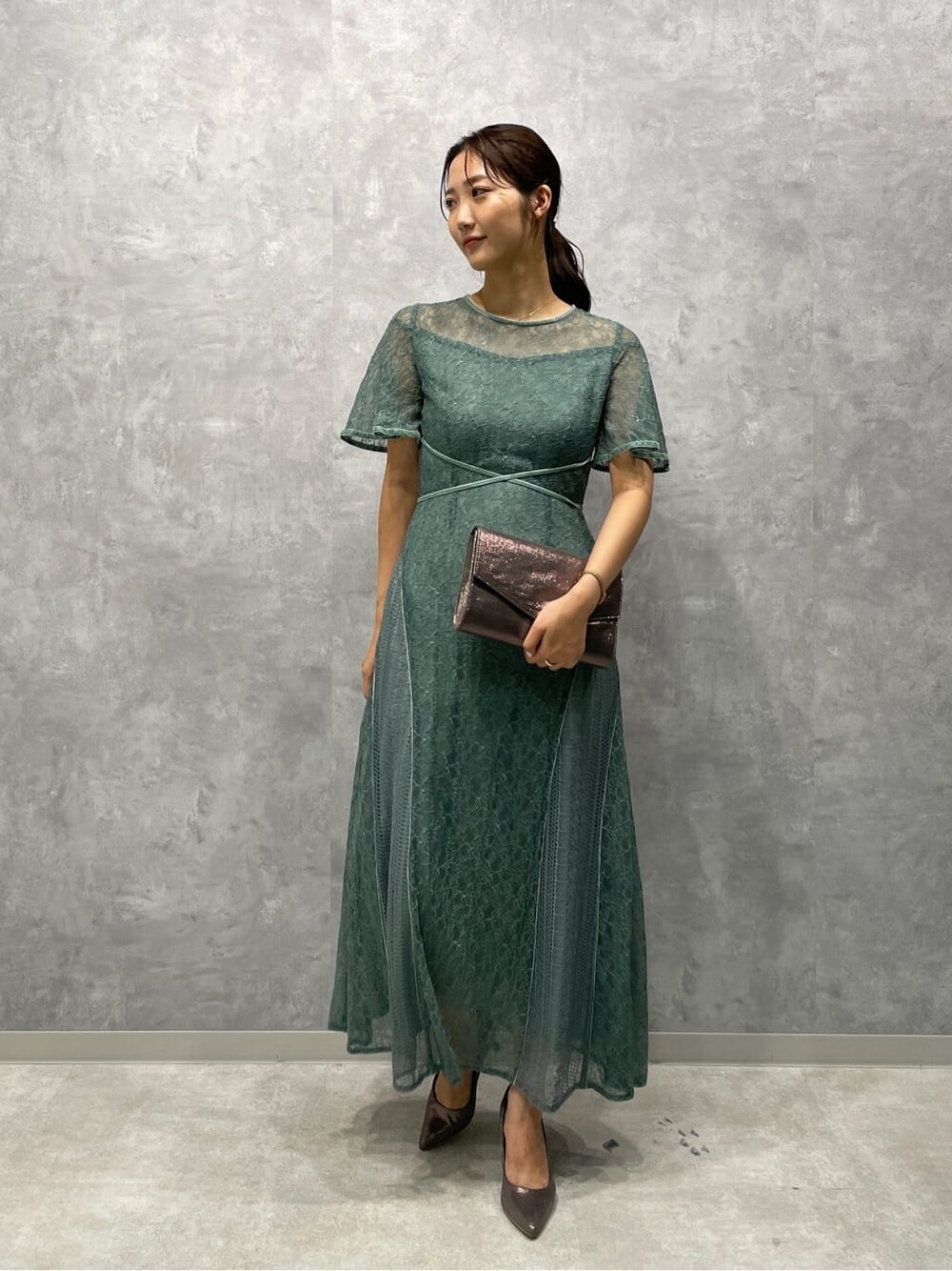 シルバー系のパンプス、シルバー系のクラッチバッグ、グリーン系のドレスを着用したレディースの夏コーディネートの3枚目の写真