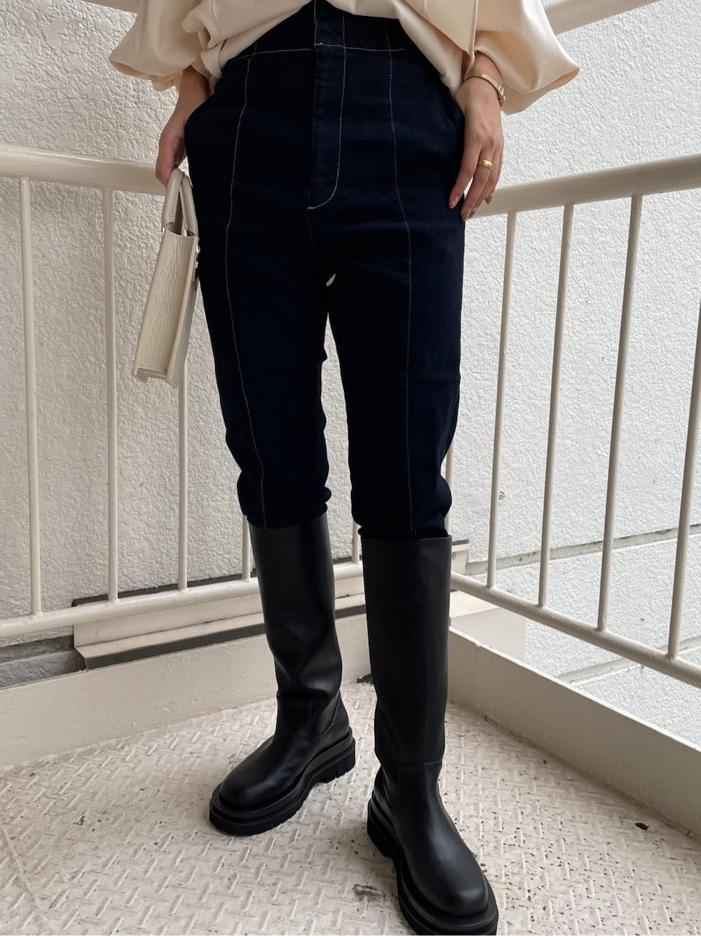 ブラック系のブーツ、ホワイト系のショルダーバッグ、ブルー系のデニムパンツを着用したレディースの秋コーディネートの8枚目の写真