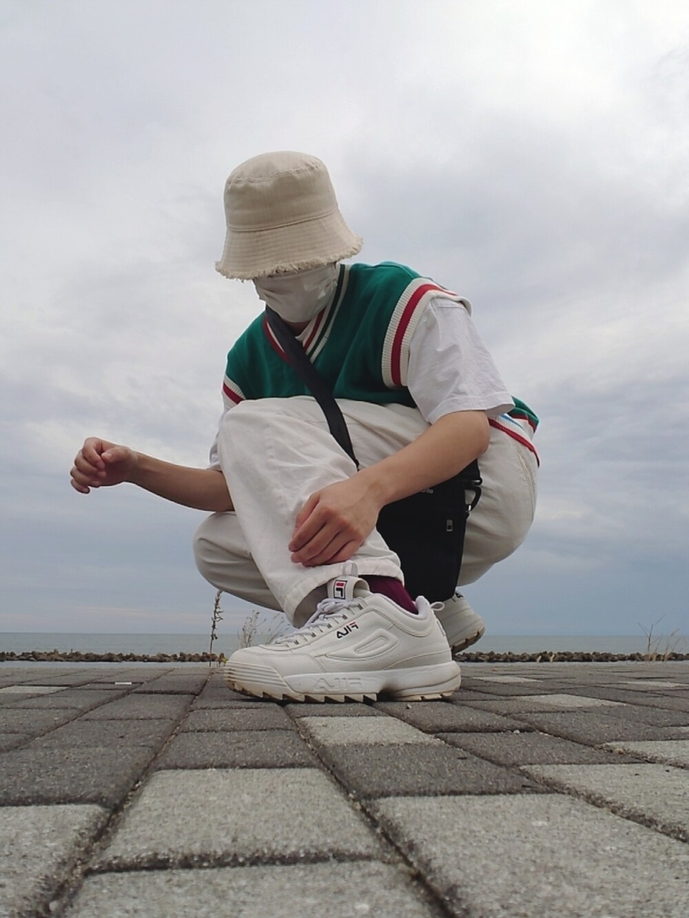 ホワイト系のスニーカー、ブラック系のショルダーバッグ、グリーン系のベストを着用したメンズの秋コーディネートの2枚目の写真