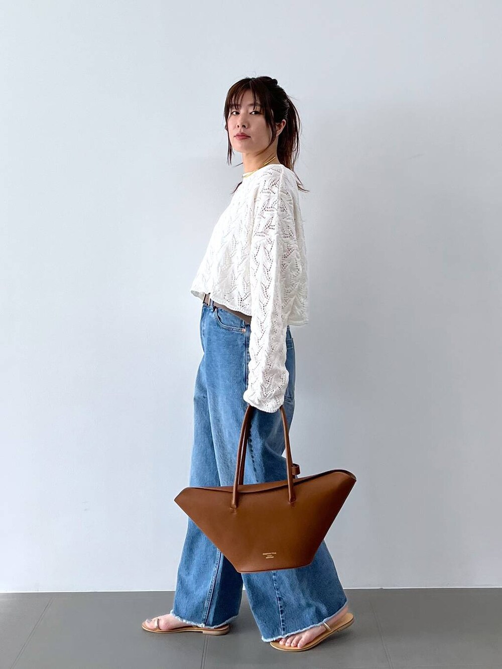 ブルー系のデニムパンツ、イエロー系のハンドバッグ、グレー系のベルトを着用したレディースの春コーディネートの5枚目の写真