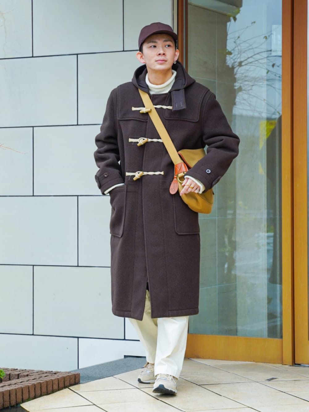 ブラウン系のダッフルコート、ホワイト系のニット/セーター、ベージュ系のショルダーバッグを着用したメンズの冬コーディネートの2枚目の写真