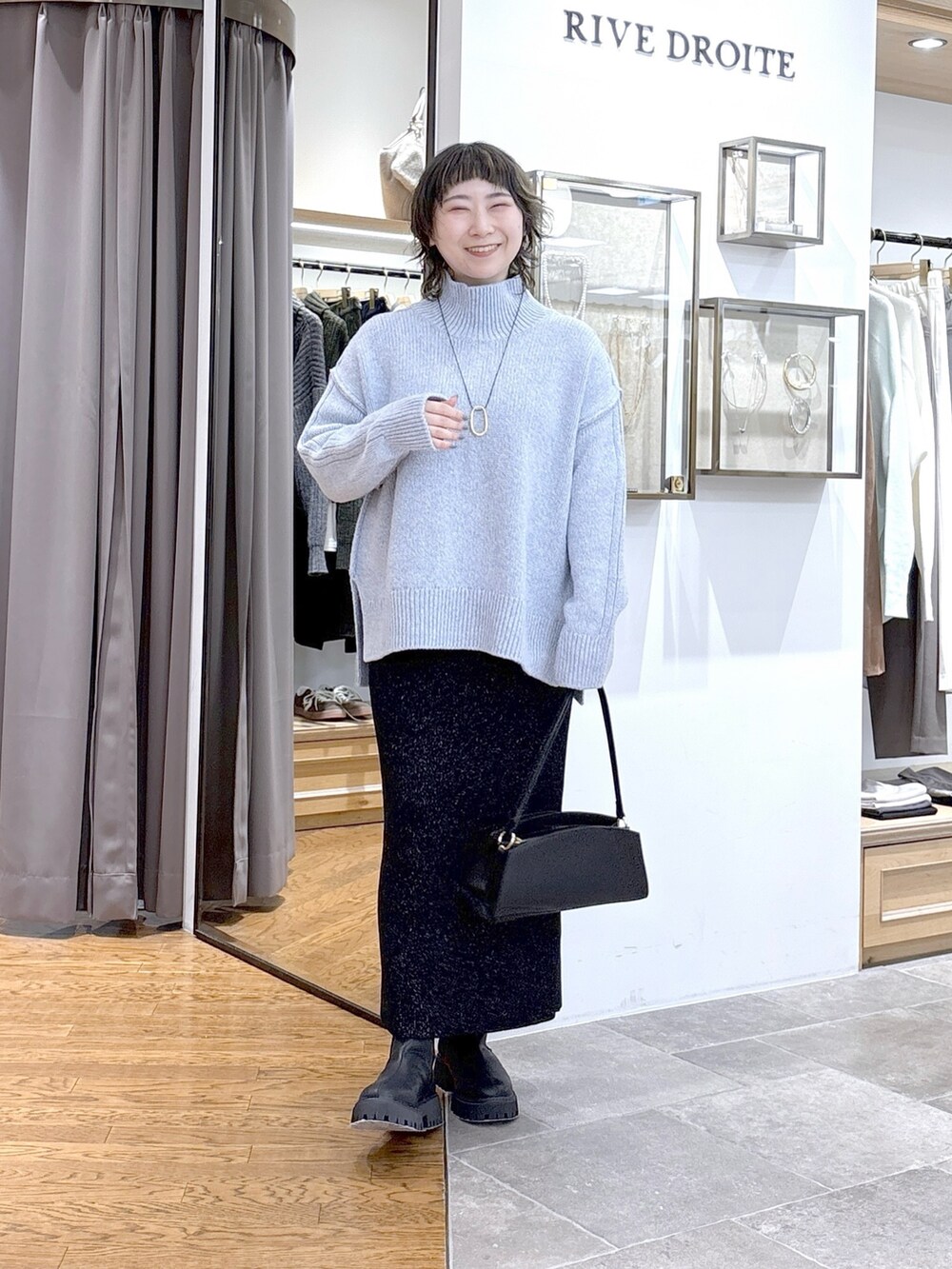 ブルー系のニット/セーター、ブルー系のピーコート、ブラック系のハンドバッグを着用したレディースの秋コーディネートの2枚目の写真