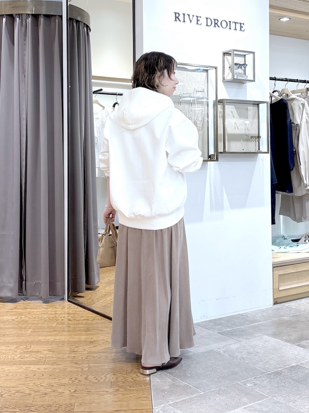 ホワイト系のパーカー、ベージュ系のトートバッグ、ブラウン系のスカートを着用したレディースの春コーディネートの3枚目の写真
