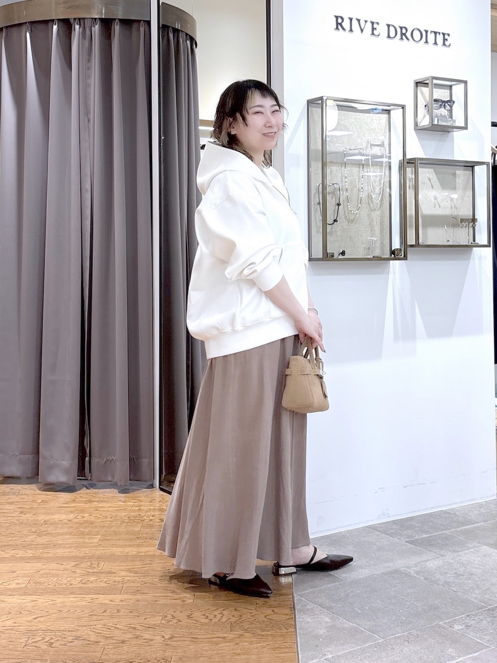 ホワイト系のパーカー、ベージュ系のトートバッグ、ブラウン系のスカートを着用したレディースの春コーディネートの2枚目の写真