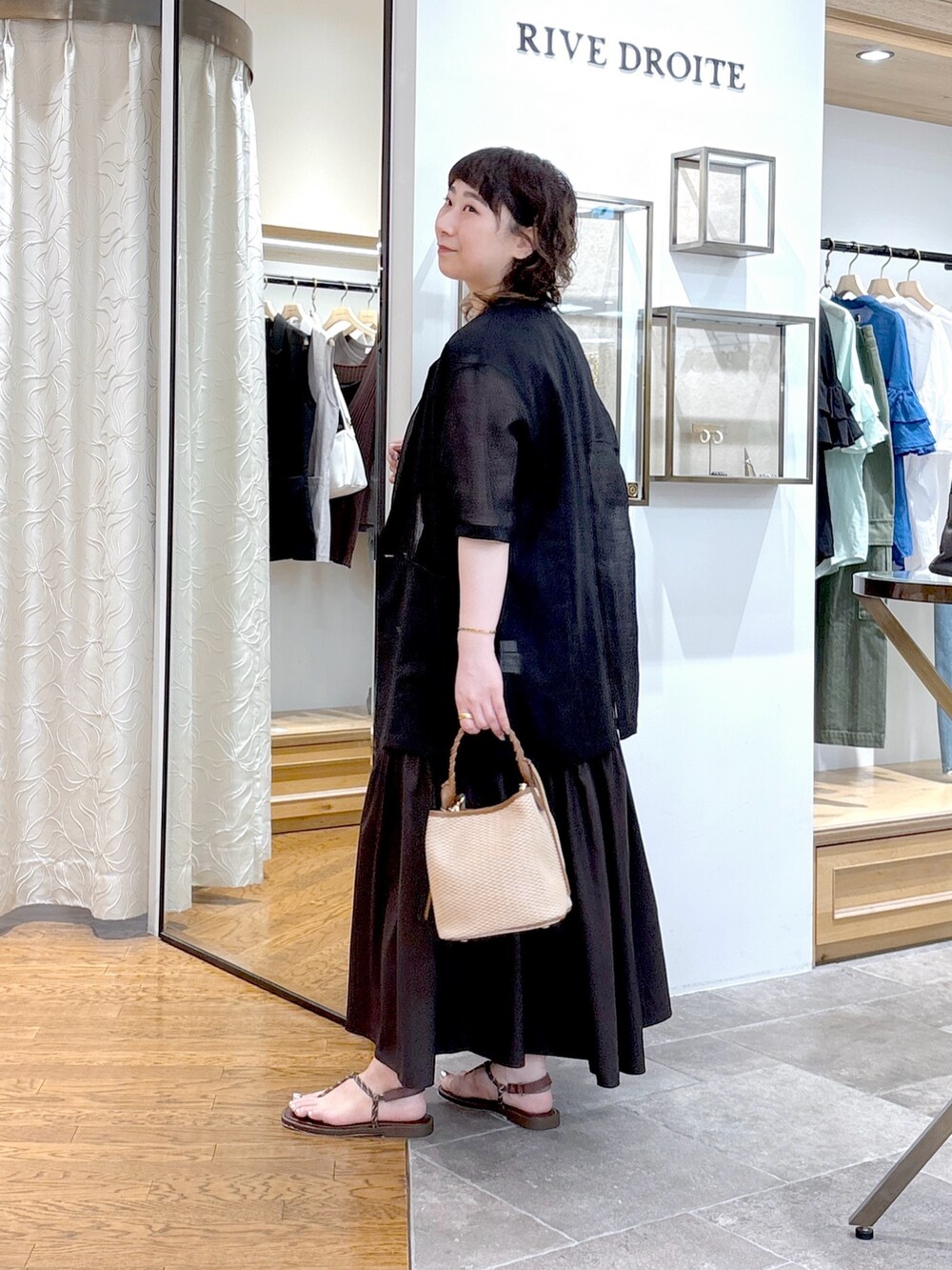 ブラック系のテーラードジャケット、ブラウン系のワンピース、ブラウン系のハンドバッグを着用したレディースの夏コーディネートの2枚目の写真