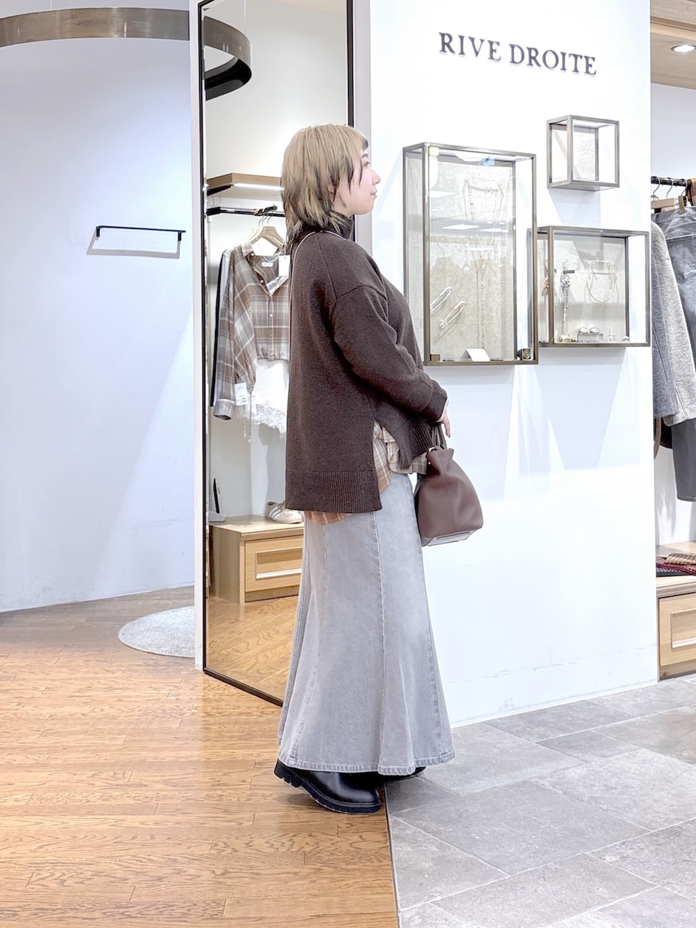 ブラウン系のニット/セーター、ベージュ系のシャツ/ブラウス、グレー系のデニムスカートを着用したレディースの秋コーディネートの2枚目の写真