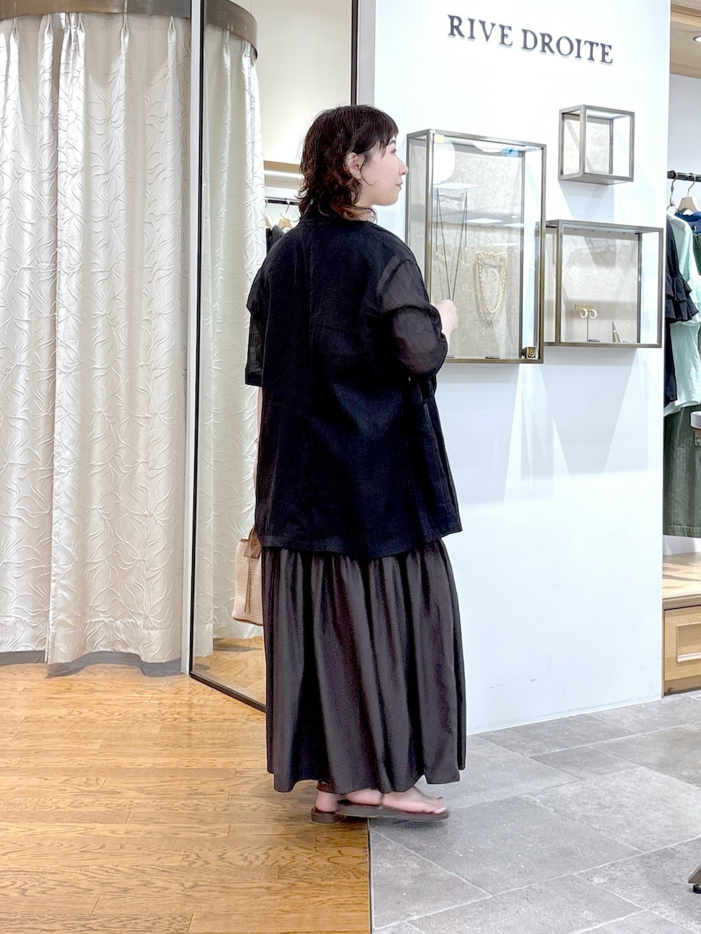 ブラック系のテーラードジャケット、ブラウン系のワンピース、ブラウン系のハンドバッグを着用したレディースの夏コーディネートの3枚目の写真