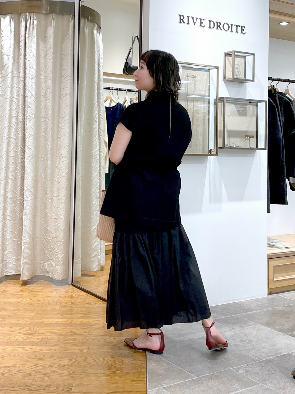 ブラック系のベスト、ブラウン系のトートバッグ、ブラック系のスカートを着用したレディースの春コーディネートの3枚目の写真