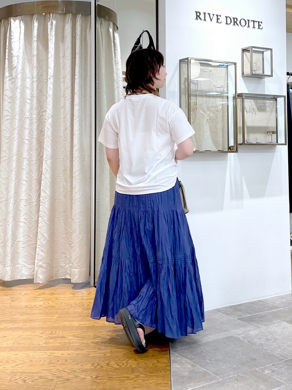 ブラック系のハンドバッグ、ブルー系のスカート、ホワイト系のTシャツ/カットソーを着用したレディースの夏コーディネートの3枚目の写真