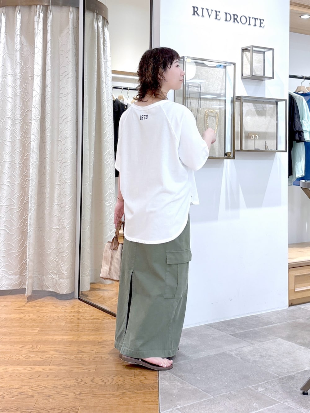 ブラウン系のハンドバッグ、ホワイト系のTシャツ/カットソー、グリーン系のスカートを着用したレディースの夏コーディネートの3枚目の写真