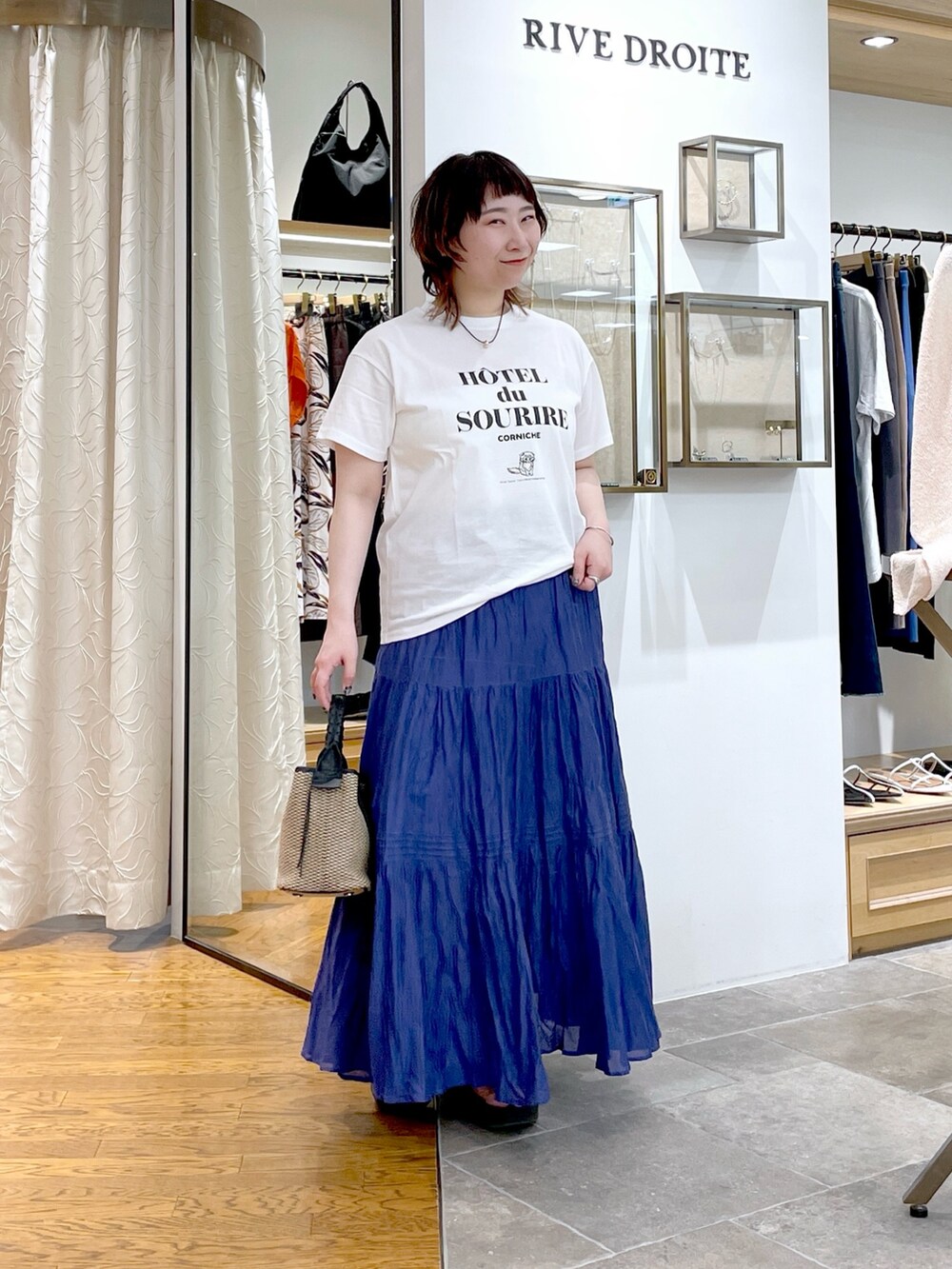 ブラック系のハンドバッグ、ブルー系のスカート、ホワイト系のTシャツ/カットソーを着用したレディースの夏コーディネートの2枚目の写真