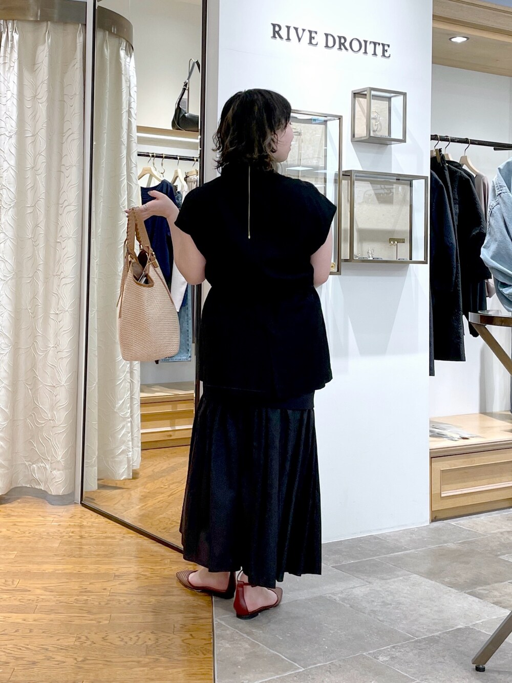 ブラック系のベスト、ブラウン系のトートバッグ、ブラック系のスカートを着用したレディースの春コーディネートの4枚目の写真