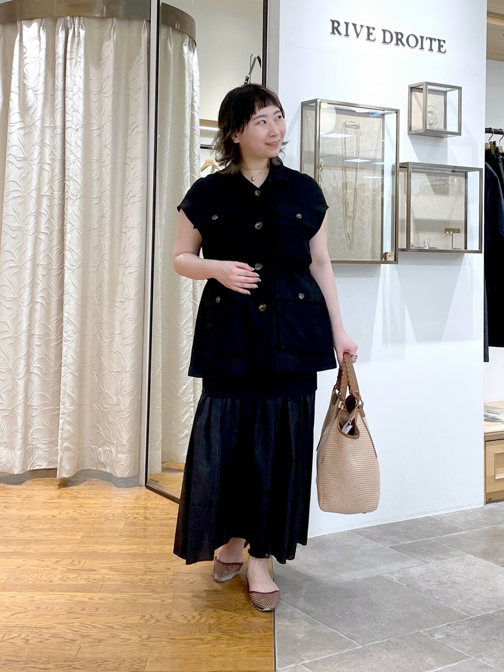 ブラック系のベスト、ブラウン系のトートバッグ、ブラック系のスカートを着用したレディースの春コーディネートの2枚目の写真