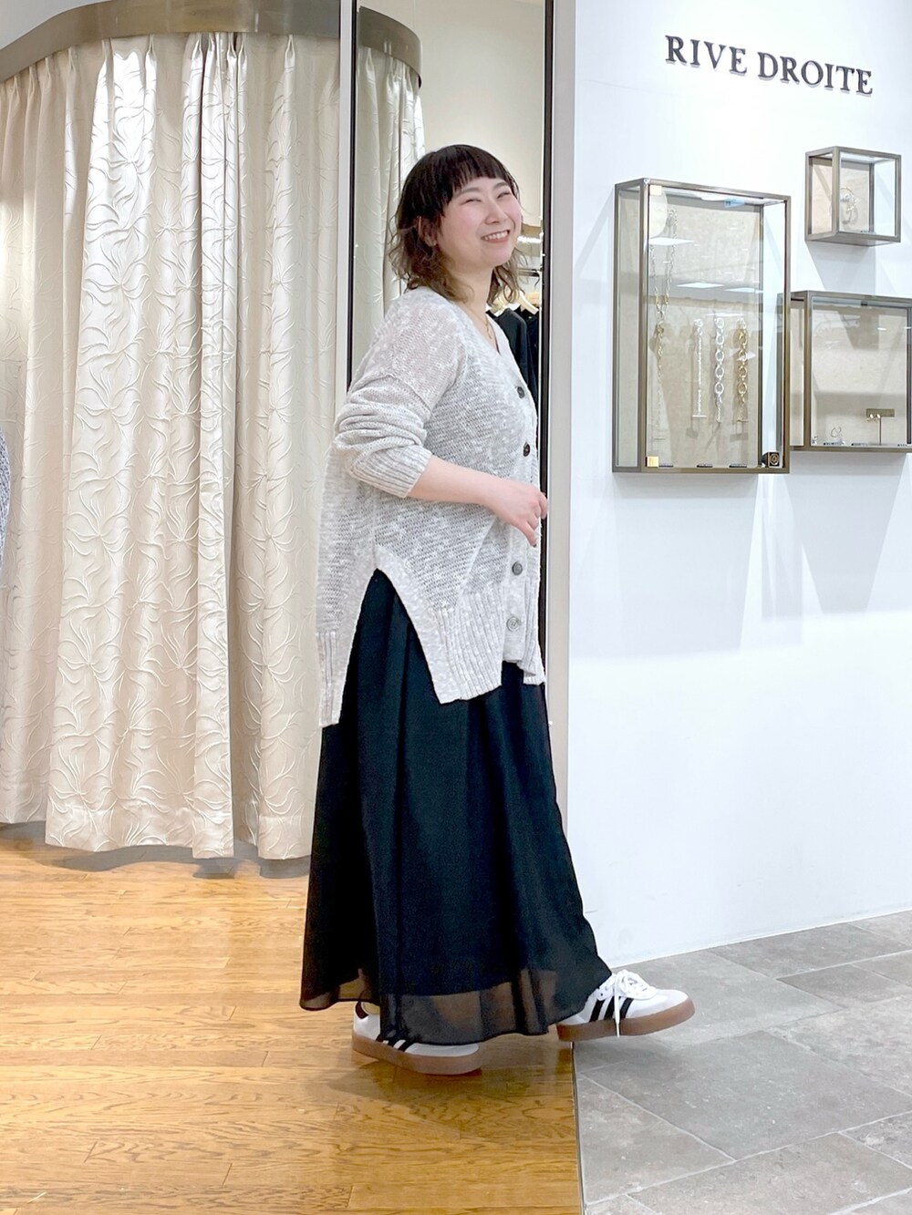 ブラック系のスカート、ホワイト系のボストンバッグ、グレー系のカーディガン/ボレロを着用したレディースの春コーディネートの2枚目の写真