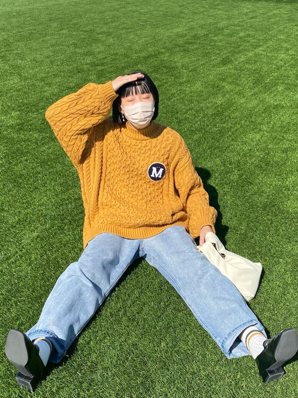 イエロー系のニット/セーター、ブルー系のデニムパンツ、ホワイト系のハンドバッグを着用したレディースの秋コーディネートの2枚目の写真