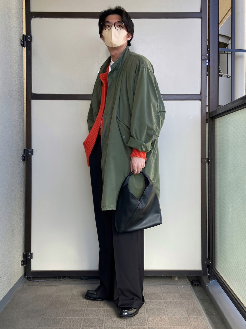 オレンジ系のカーディガン/ボレロ、ブラック系のハンドバッグ、ブラック系のスラックスを着用したメンズの冬コーディネートの2枚目の写真