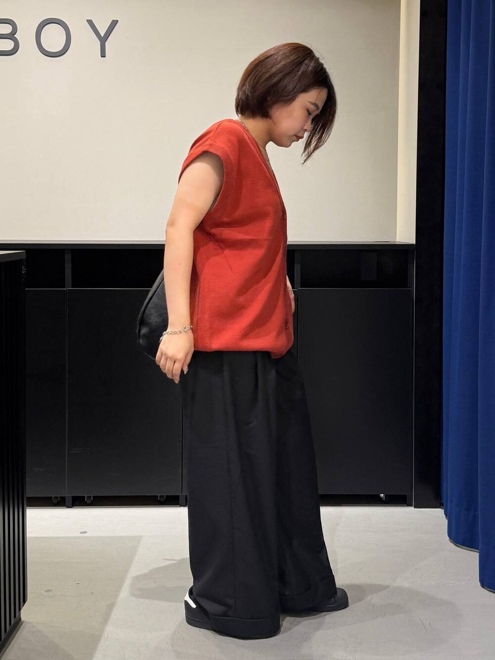 ホワイト系のキャミソール、ブラック系のスラックス、オレンジ系のベストを着用したレディースの夏コーディネートの4枚目の写真