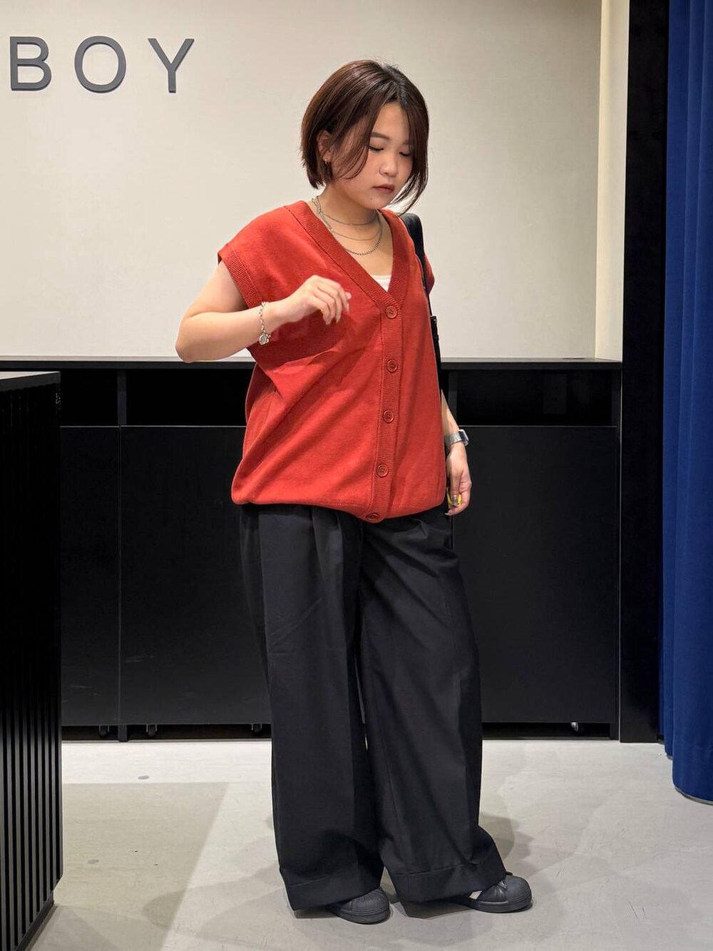 ホワイト系のキャミソール、ブラック系のスラックス、オレンジ系のベストを着用したレディースの夏コーディネートの3枚目の写真