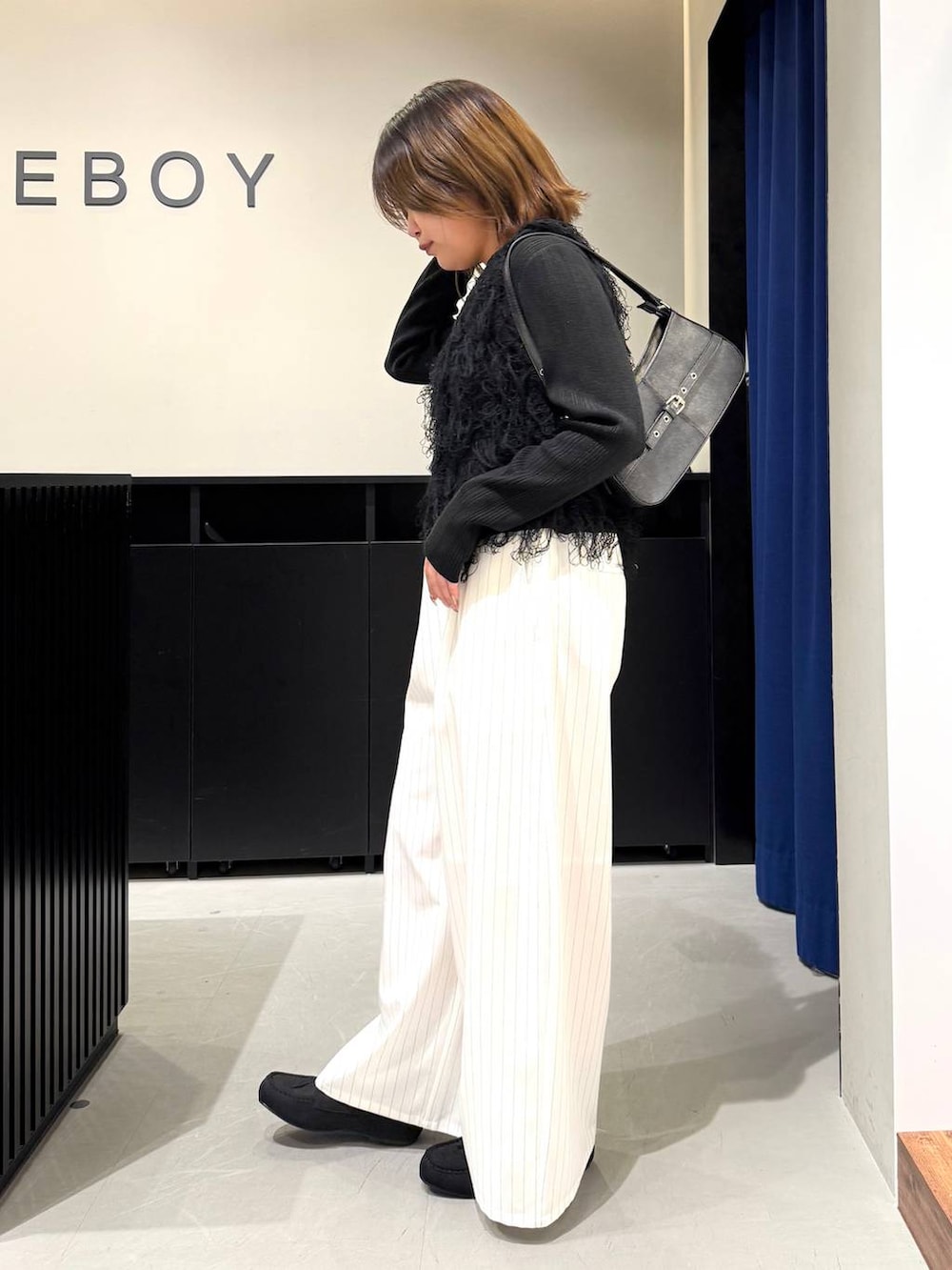 ブラック系のハンドバッグ、ブラック系のニット/セーター、ホワイト系のスラックスを着用したレディースの冬コーディネートの7枚目の写真