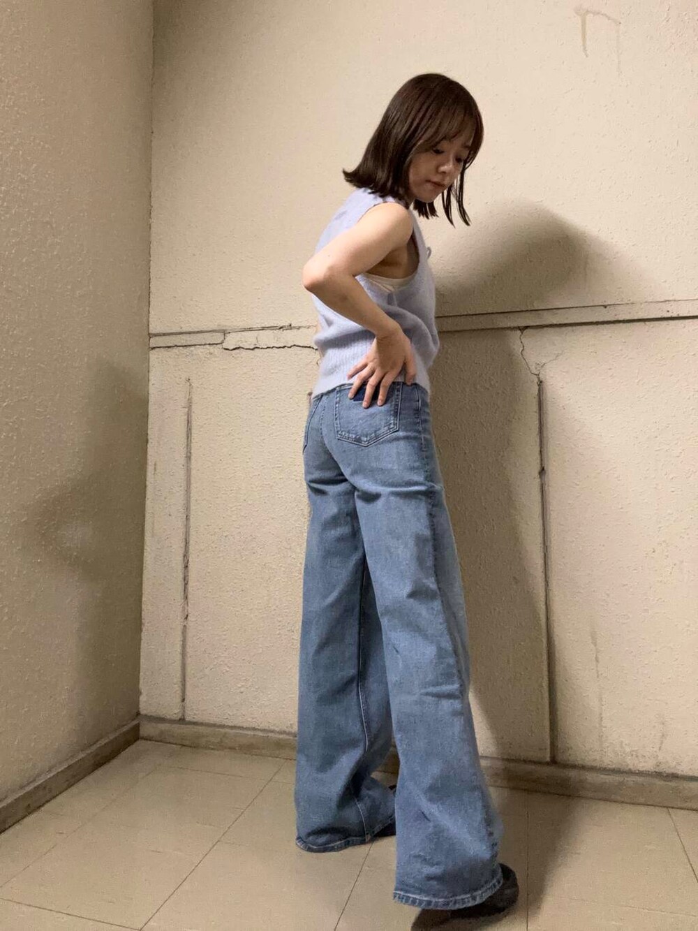 グレー系のベスト、ブラック系のスニーカー、ブルー系のデニムパンツを着用したレディースの夏コーディネートの3枚目の写真