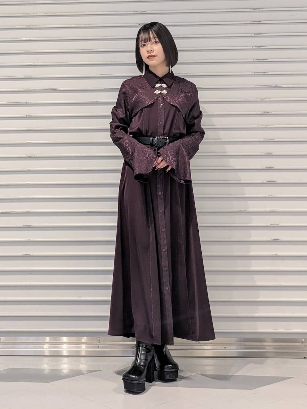 グレー系のチェスターコート、ブラック系のブーツ、レッド系のワンピースを着用したレディースの冬コーディネートの2枚目の写真