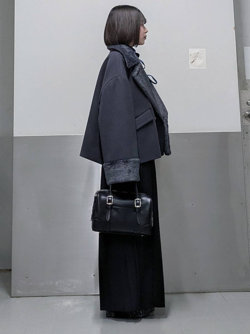 グレー系のチェスターコート、ブラック系のボストンバッグ、グレー系のブーツを着用したレディースの秋コーディネートの4枚目の写真