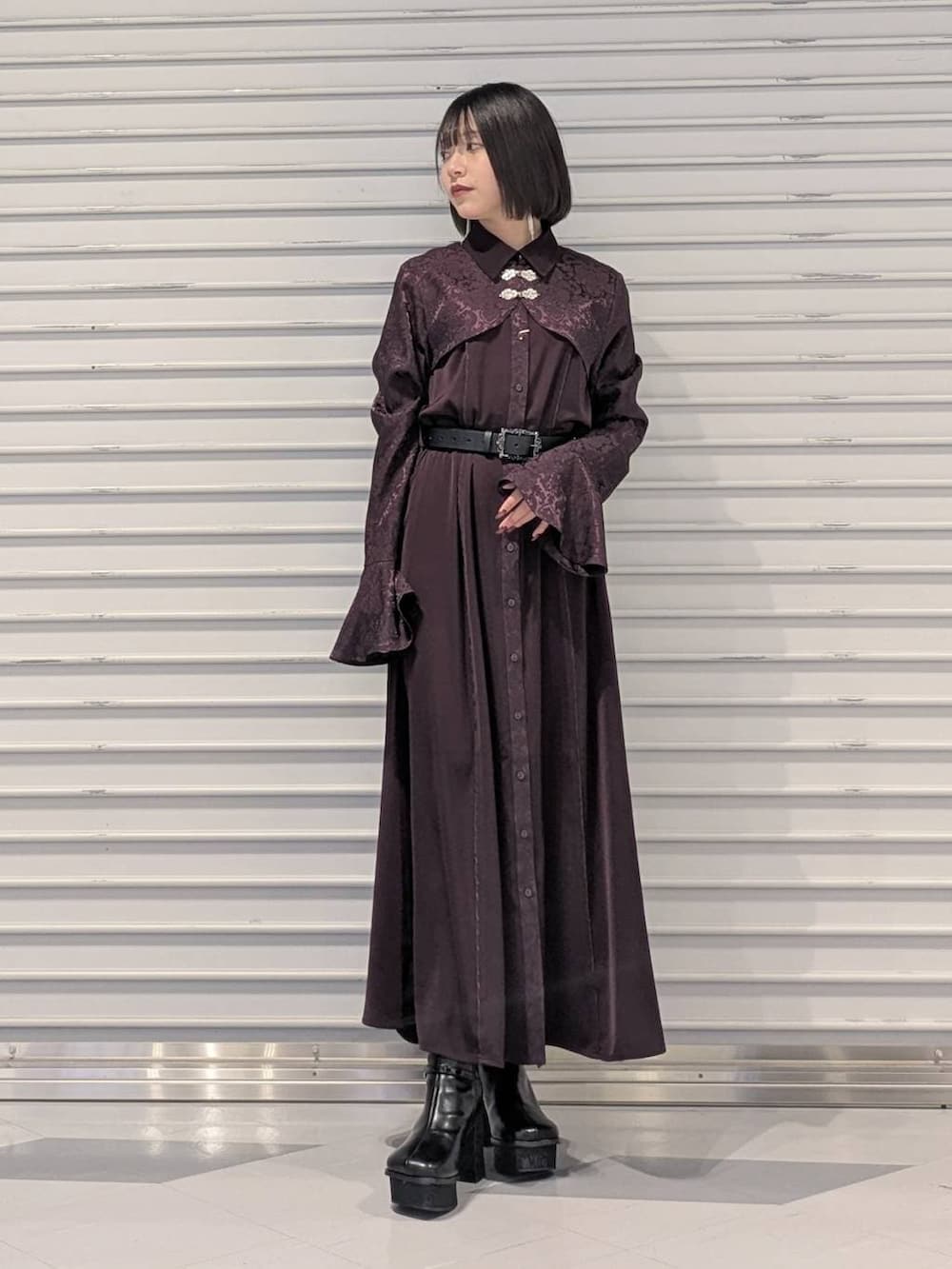 グレー系のチェスターコート、ブラック系のブーツ、レッド系のワンピースを着用したレディースの冬コーディネートの3枚目の写真