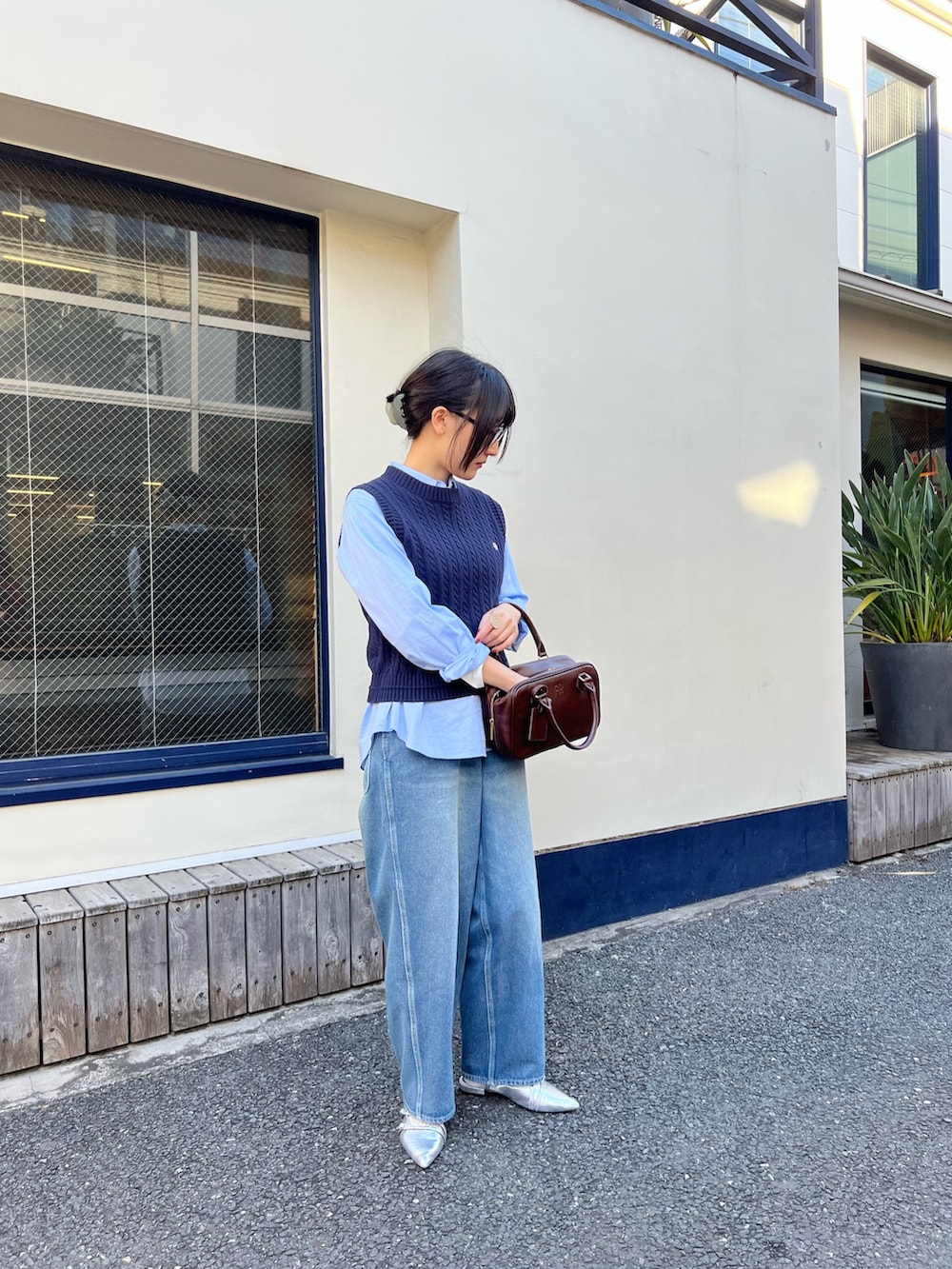 ブルー系のベスト、ブルー系のデニムパンツ、ブラウン系のハンドバッグを着用したレディースの冬コーディネートの2枚目の写真