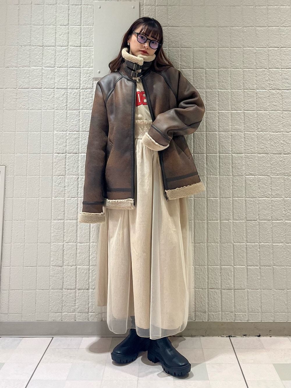 ブラウン系のムートンコート、ベージュ系のワンピース、ブラック系のブーツを着用したレディースの春コーディネートの2枚目の写真